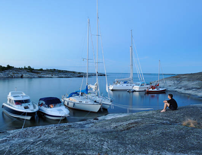 Veneet satamassa, poika istuu kalliolla